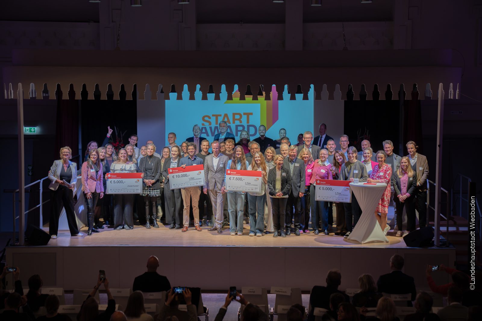 The prize winners, jury and organisers of the StartAward Wiesbaden 2026 gathered on the Tattersall stage with their cheques.